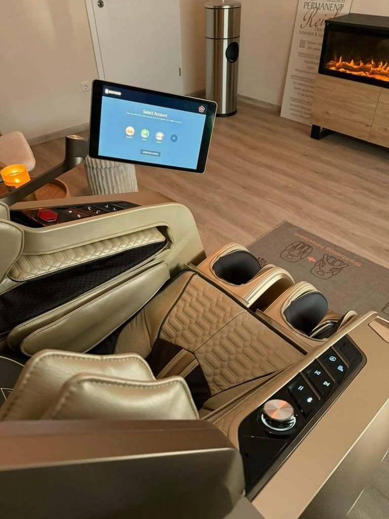 Blick aus dem Massagesessel auf Tablet-Steuerung und Kaminfeuer